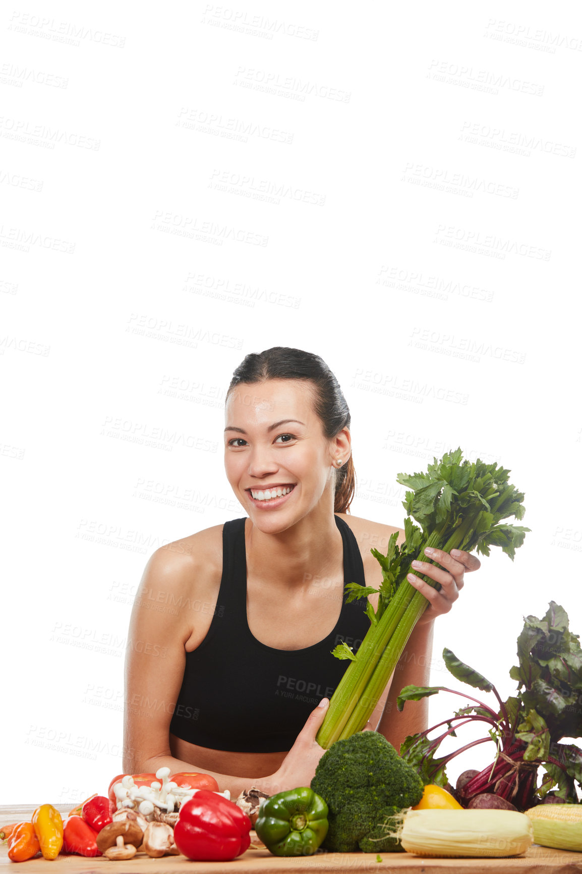 Buy stock photo Studio portrait of an attractive young woman posing with a table full of vegetables against a white background