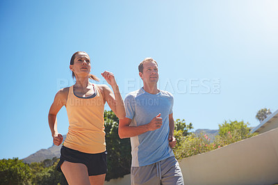 Buy stock photo Low angle shot of a happy couple jogging together in their neighborhood
