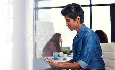 Buy stock photo Cropped shot of a young businesswoman working on a digital tablet with her colleagues in the background