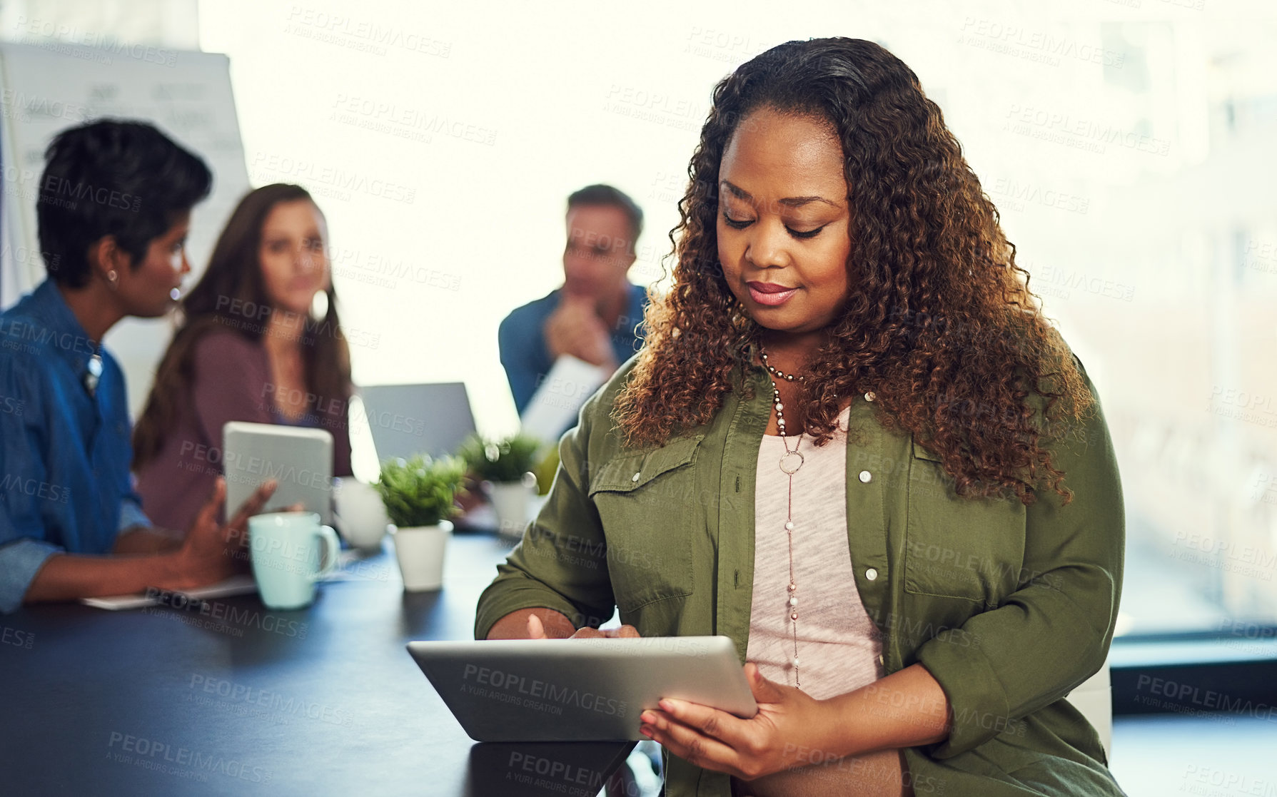 Buy stock photo Cropped shot of a young businesswoman working on a digital tablet with her colleagues in the background