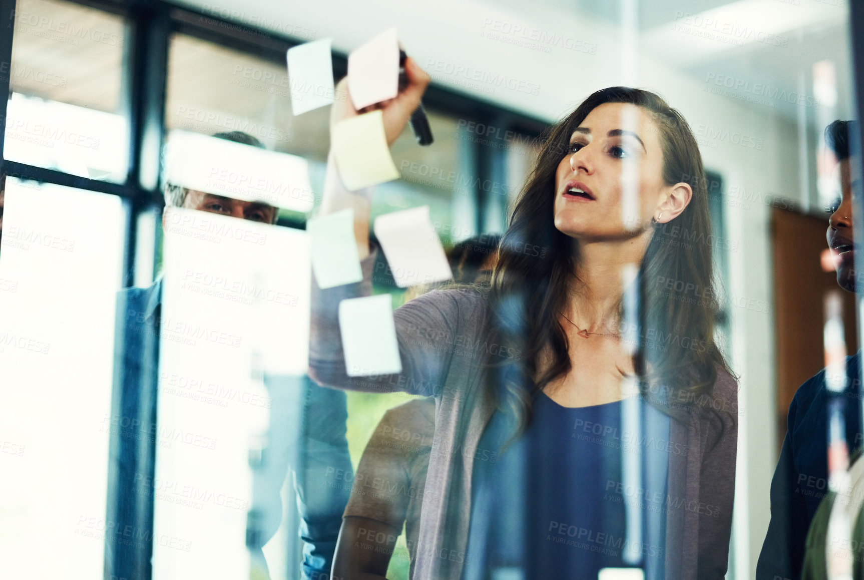 Buy stock photo Cropped shot of a group of businesspeople brainstorming with notes on a glass wall in an office