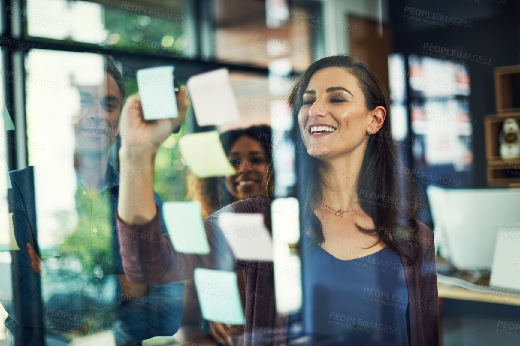 Buy stock photo Cropped shot of a group of businesspeople brainstorming with notes on a glass wall in an office