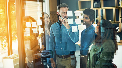 Buy stock photo Cropped shot of a group of businesspeople brainstorming with notes on a glass wall in an office