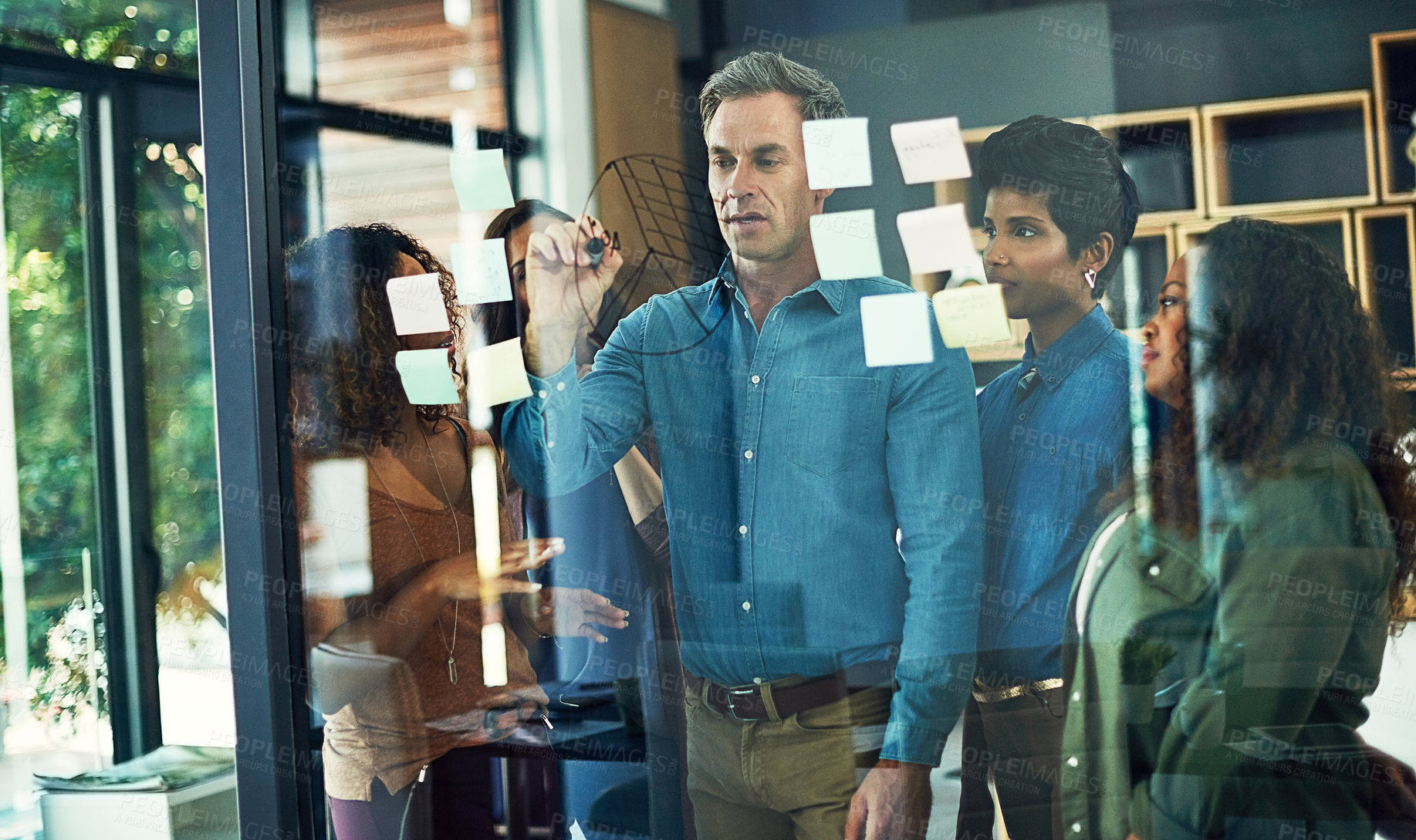 Buy stock photo Cropped shot of a group of businesspeople brainstorming with notes on a glass wall in an office