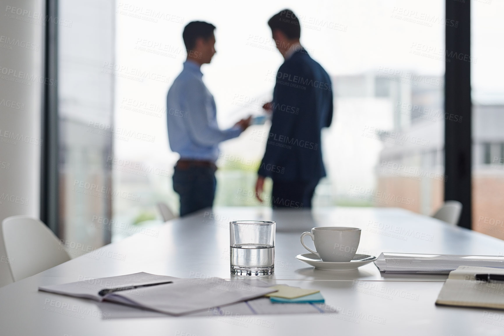 Buy stock photo Shot of paperwork on a table in an office with two businessmen having a discussion in the background