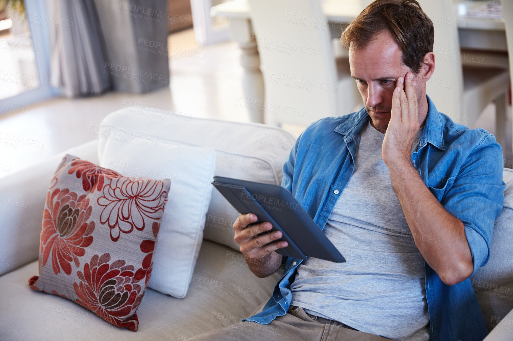 Buy stock photo Shot of a man looking frustrated while using a digital tablet at home