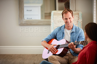 Buy stock photo Shot of a man playing the guitar for his wife at home