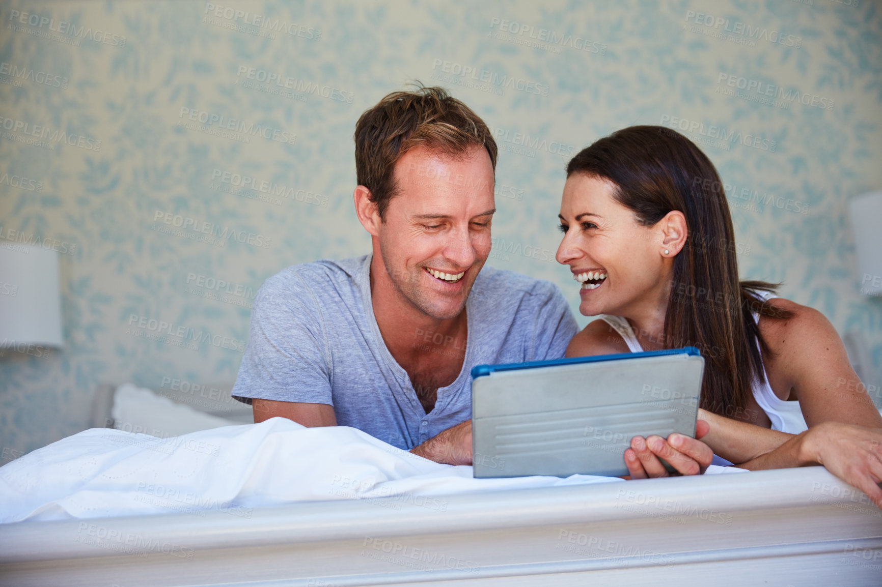 Buy stock photo Tablet, relax and laugh with couple in bed for video, comedy or streaming movie on internet together. Tech, man and woman in bedroom at home for show, funny film and chill with partner in morning