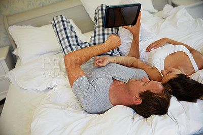 Buy stock photo Shot of a mature couple using a digital tablet while relaxing in bed together