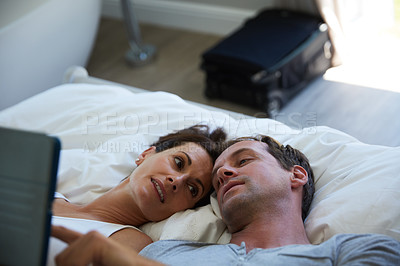 Buy stock photo Shot of a mature couple using a digital tablet while relaxing in bed together