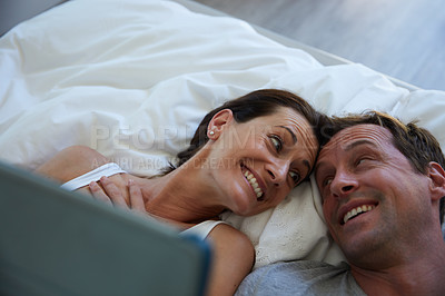 Buy stock photo Shot of a mature couple using a digital tablet while relaxing in bed together