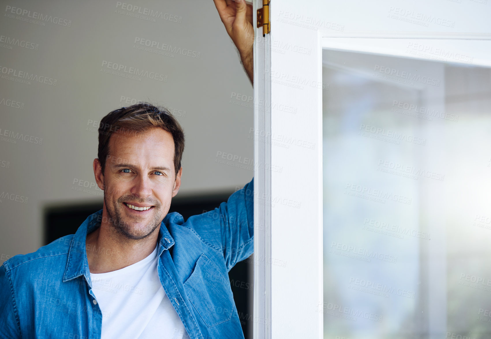 Buy stock photo Cropped portrait of a handsome man leaning against a door at home