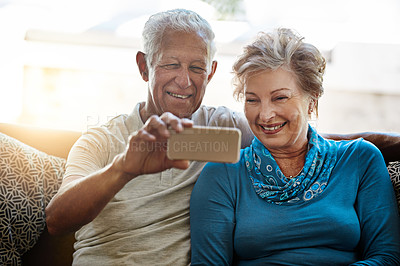 Buy stock photo Shot of a happy senior couple taking a selfie together on the sofa at home