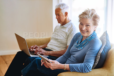Buy stock photo Portrait of a senior woman using a digital tablet while her husband uses a laptop on the sofa at home