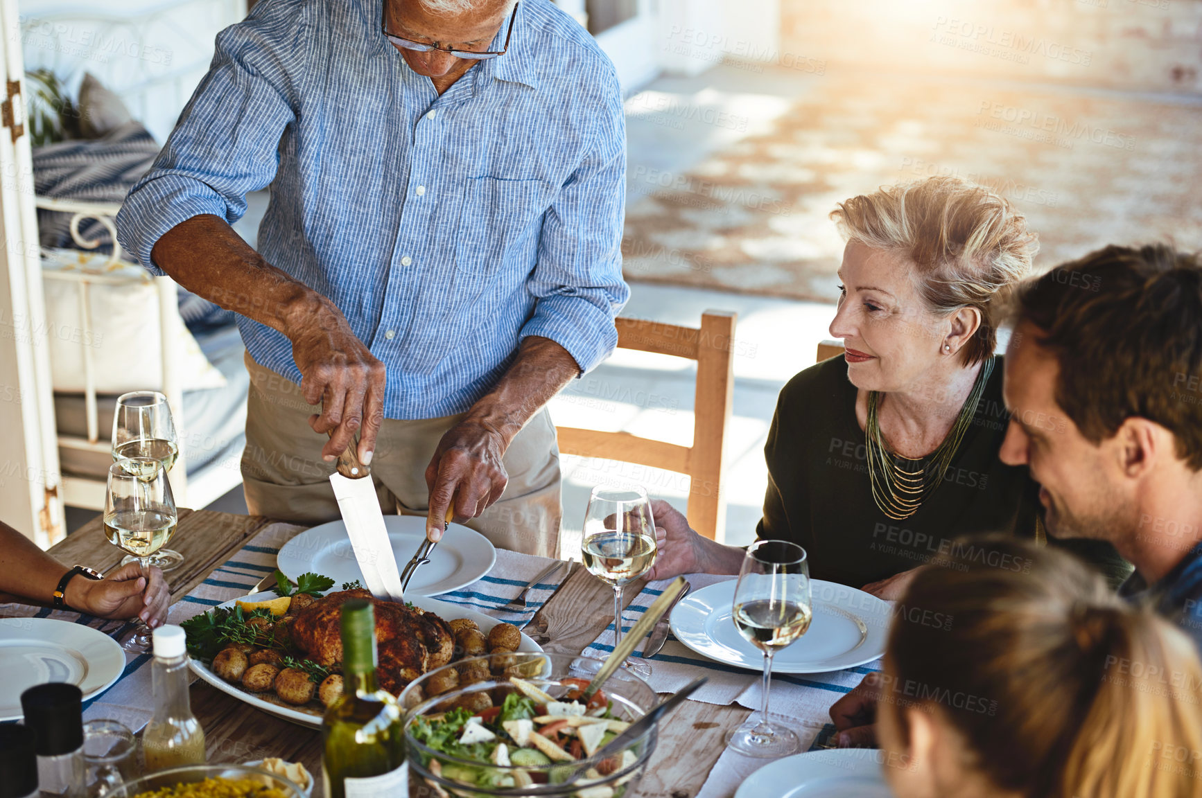 Buy stock photo Shot of a mature man carving a roast while enjoying lunch with his family outside