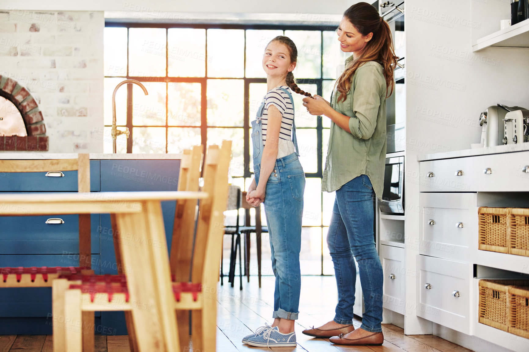 Buy stock photo Shot of a happy mother braiding her daughter’s hair at home