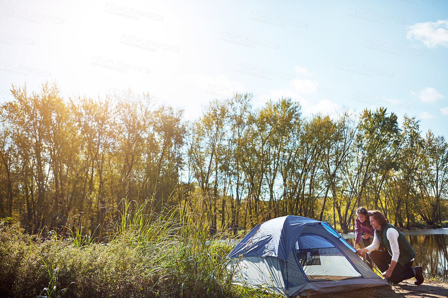 Buy stock photo Shot of an adventurous setting up their tent by the lake