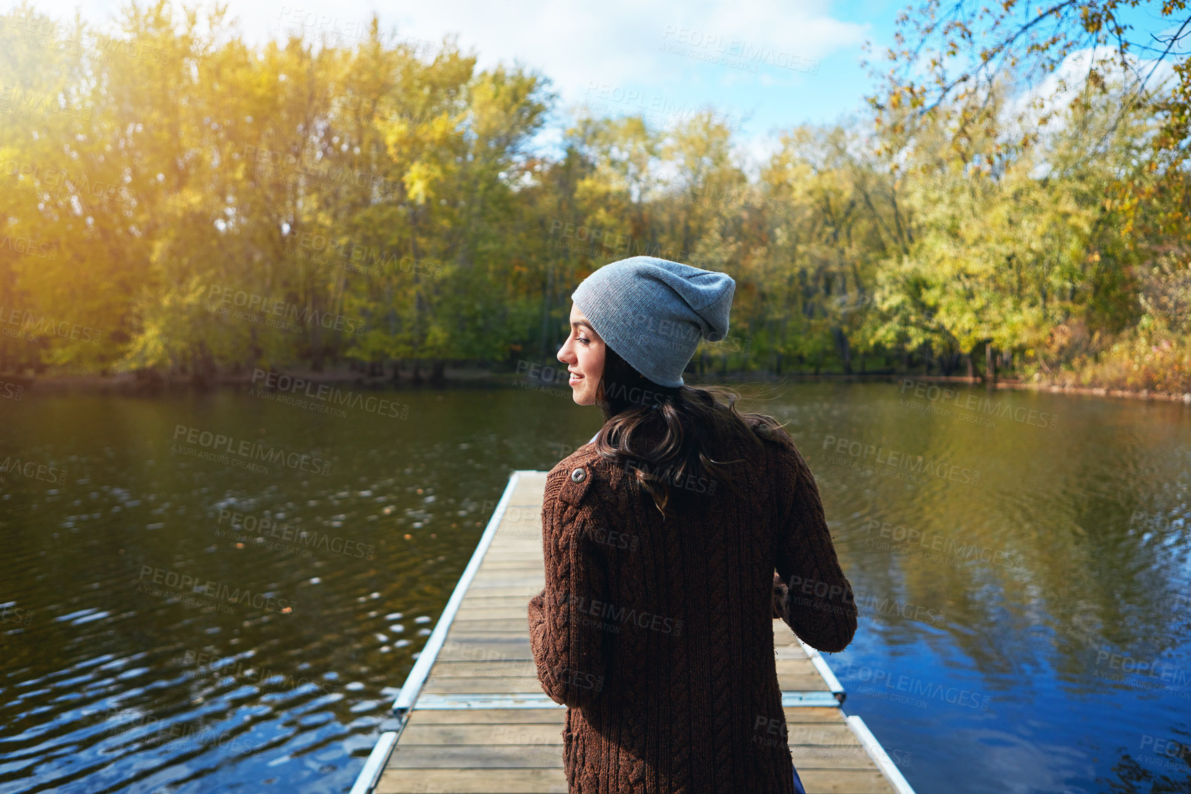 Buy stock photo Shot of a happy young woman standing on a pier next to a lake