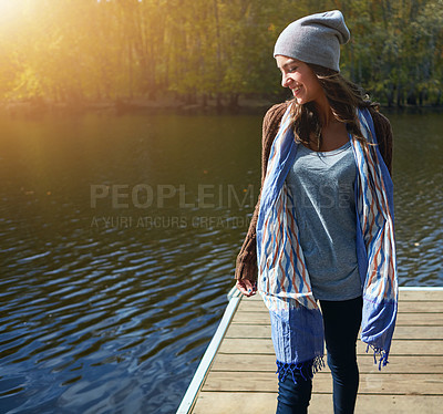 Buy stock photo Shot of a happy young woman standing on a pier next to a lake