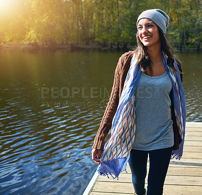 Buy stock photo Shot of a happy young woman standing on a pier next to a lake