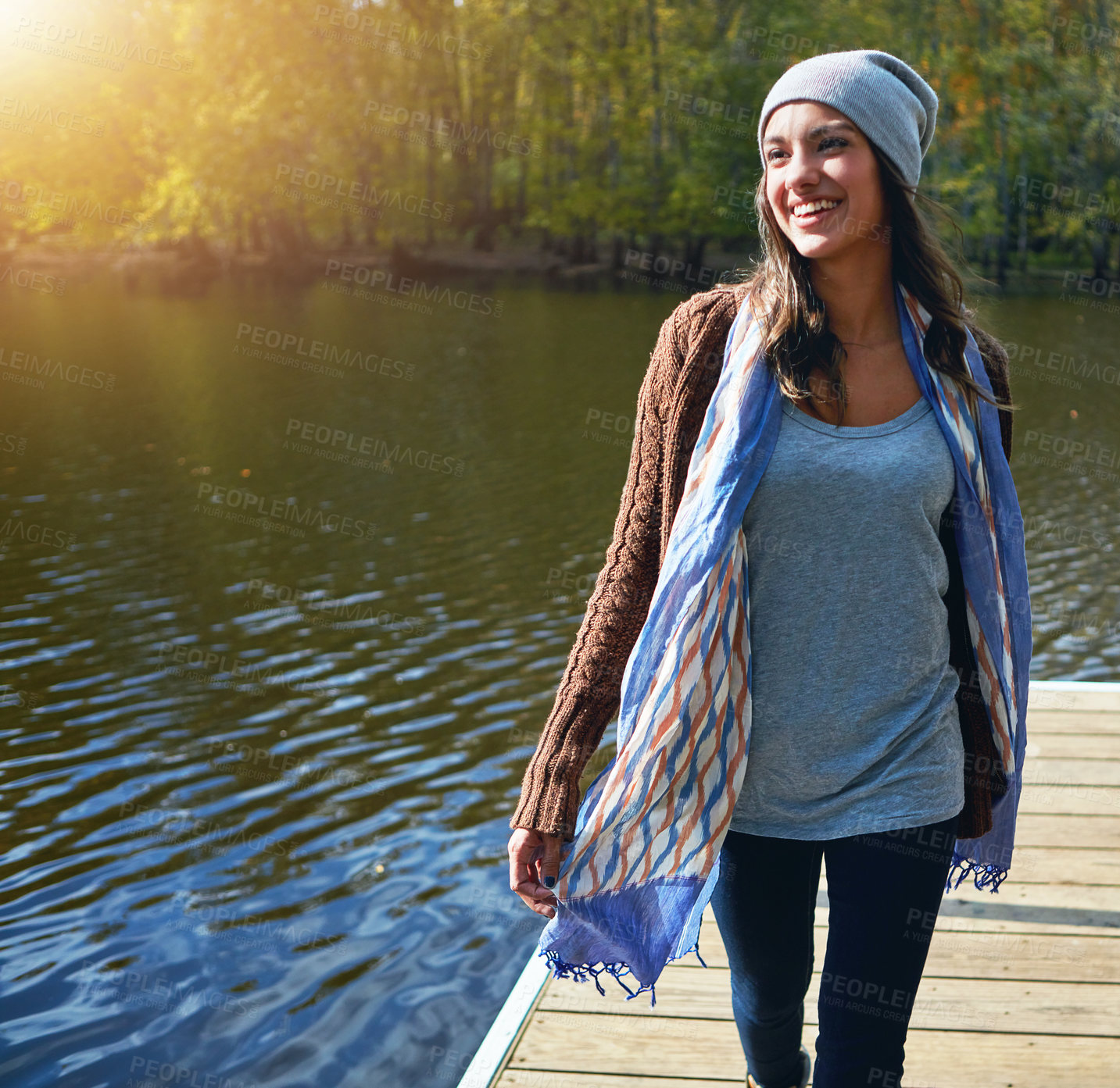 Buy stock photo Shot of a happy young woman standing on a pier next to a lake