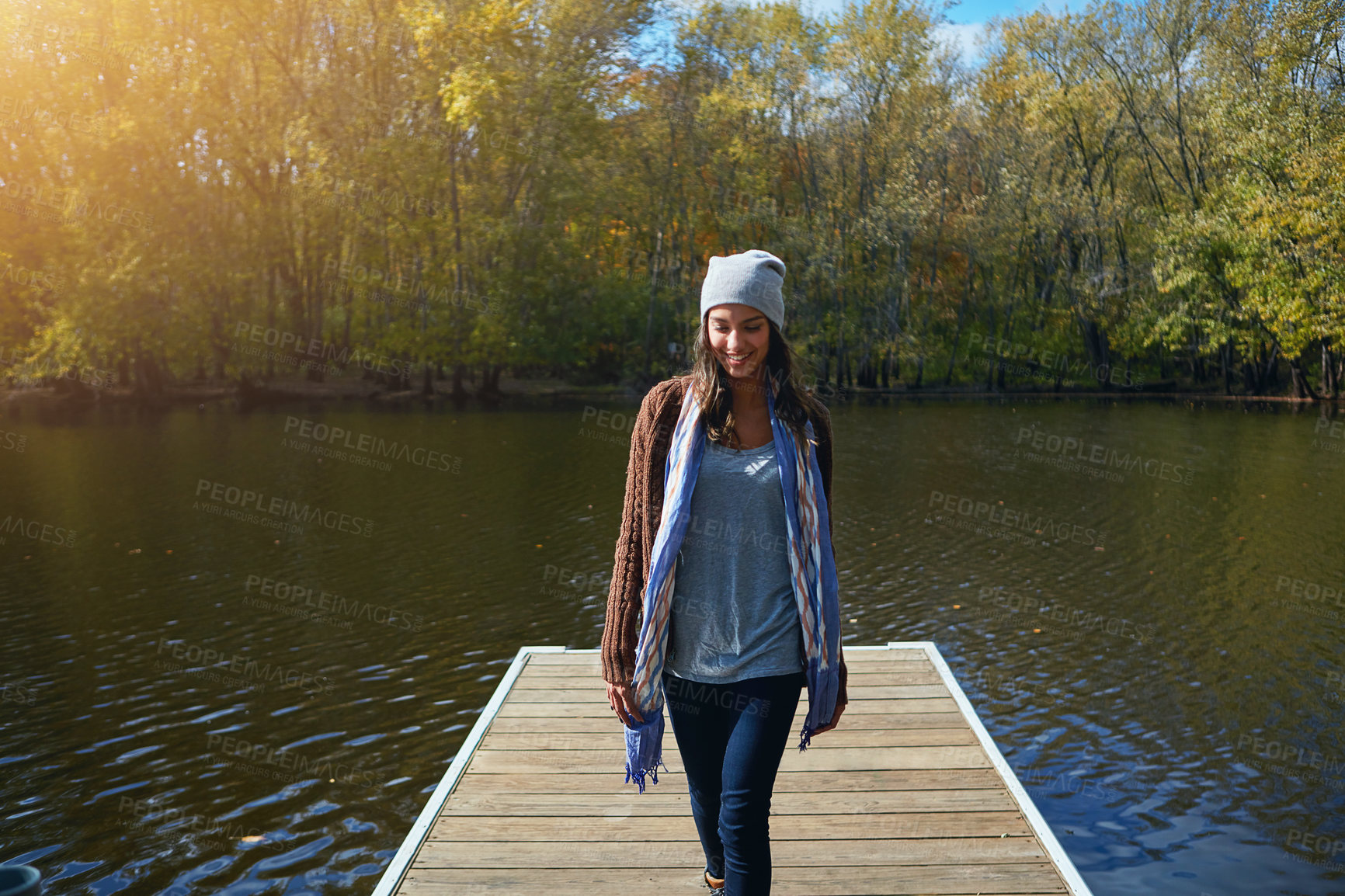 Buy stock photo Shot of a happy young woman standing on a pier next to a lake