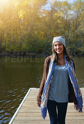 Buy stock photo Shot of a happy young woman standing on a pier next to a lake