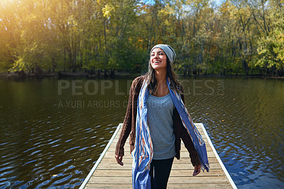 Buy stock photo Shot of a happy young woman standing on a pier next to a lake