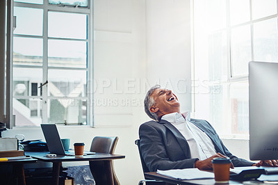 Buy stock photo Shot of a mature businessman laughing while working on a computer in an office