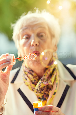 Buy stock photo Shot of a fun-loving senior woman blowing bubbles outside on a sunny day