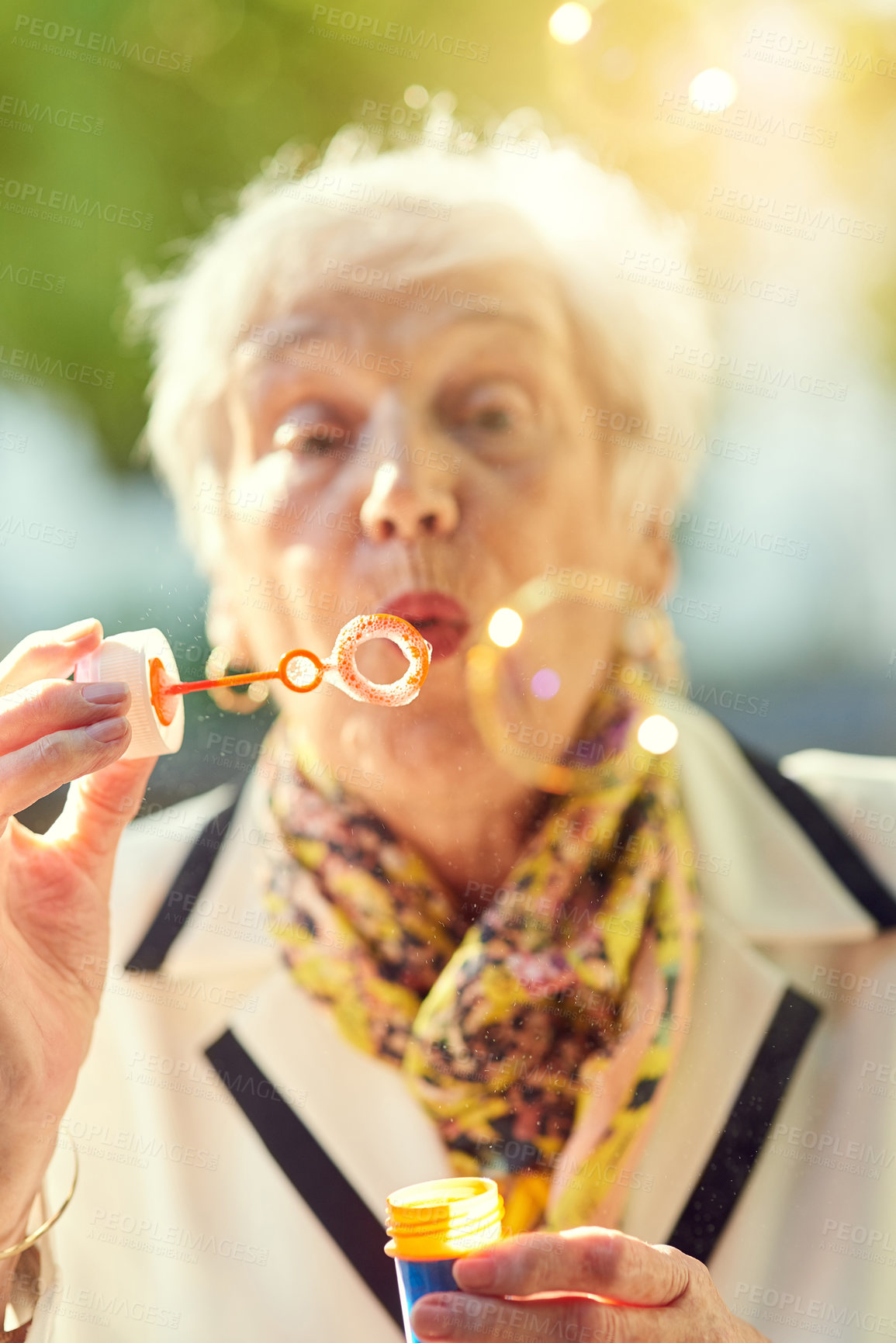 Buy stock photo Shot of a fun-loving senior woman blowing bubbles outside on a sunny day