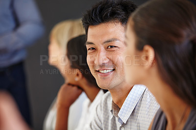 Buy stock photo Shot of an Asian man sitting at a table with his coworkers out of focus