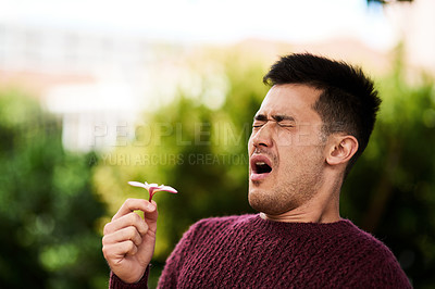 Buy stock photo Cropped shot of a young man sneezing after smelling a flower