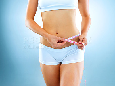 Buy stock photo Cropped studio shot of a fit young woman measuring her waist against a blue background
