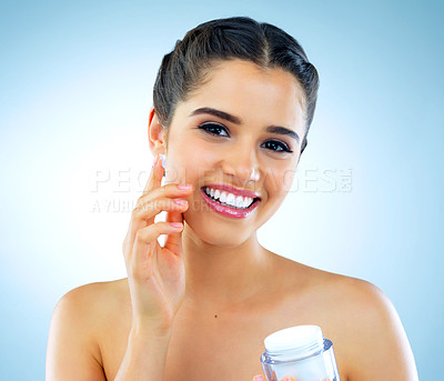 Buy stock photo Studio shot of a beautiful young woman applying moisturizer to her face against a blue background