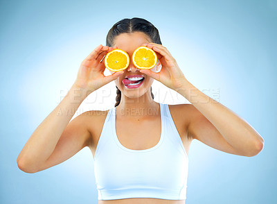 Buy stock photo Studio shot of a healthy young woman holding up oranges in front of her eyes against a blue background