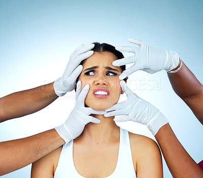 Buy stock photo Studio shot of an anxious young woman with gloved hands poking at her face against a blue background