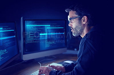 Buy stock photo Shot of a focussed computer hacker using a computer in the dark