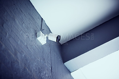 Buy stock photo Low angle shot of a security camera mounted on the wall outside a building