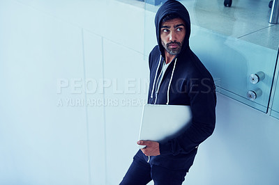 Buy stock photo Shot of a shady-looking young man holding a laptop in an office