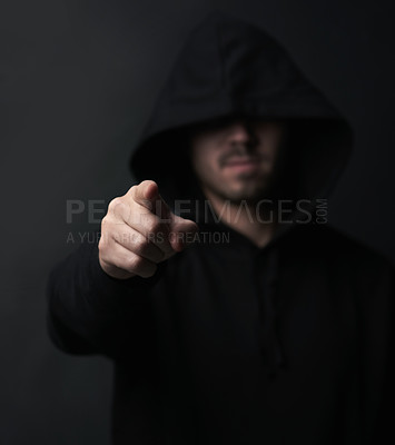 Buy stock photo Shot of an unidentifiable hooded man pointing while standing against a dark background