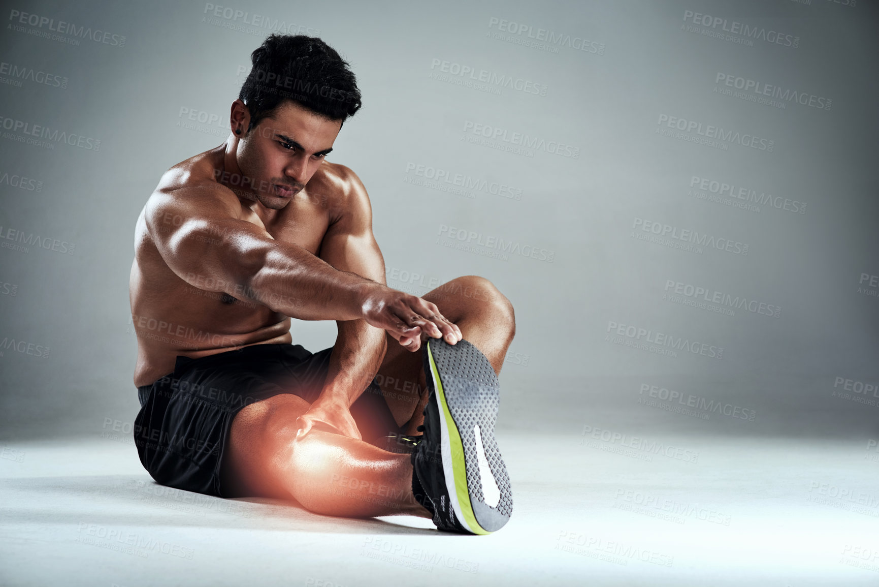 Buy stock photo Full length shot of a sporty young man stretching his calf against a grey background