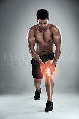 Buy stock photo Full length shot of a sporty young man nursing an injured knee against a grey background