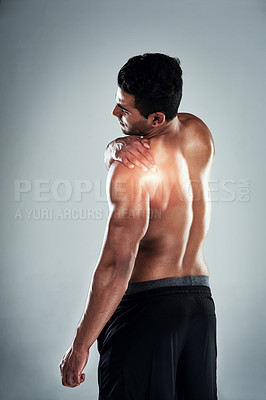 Buy stock photo Shot of a sporty young man holding his shoulder in pain against a grey background