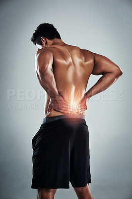 Buy stock photo Rearview shot of a sporty young man holding his back in pain against a grey background