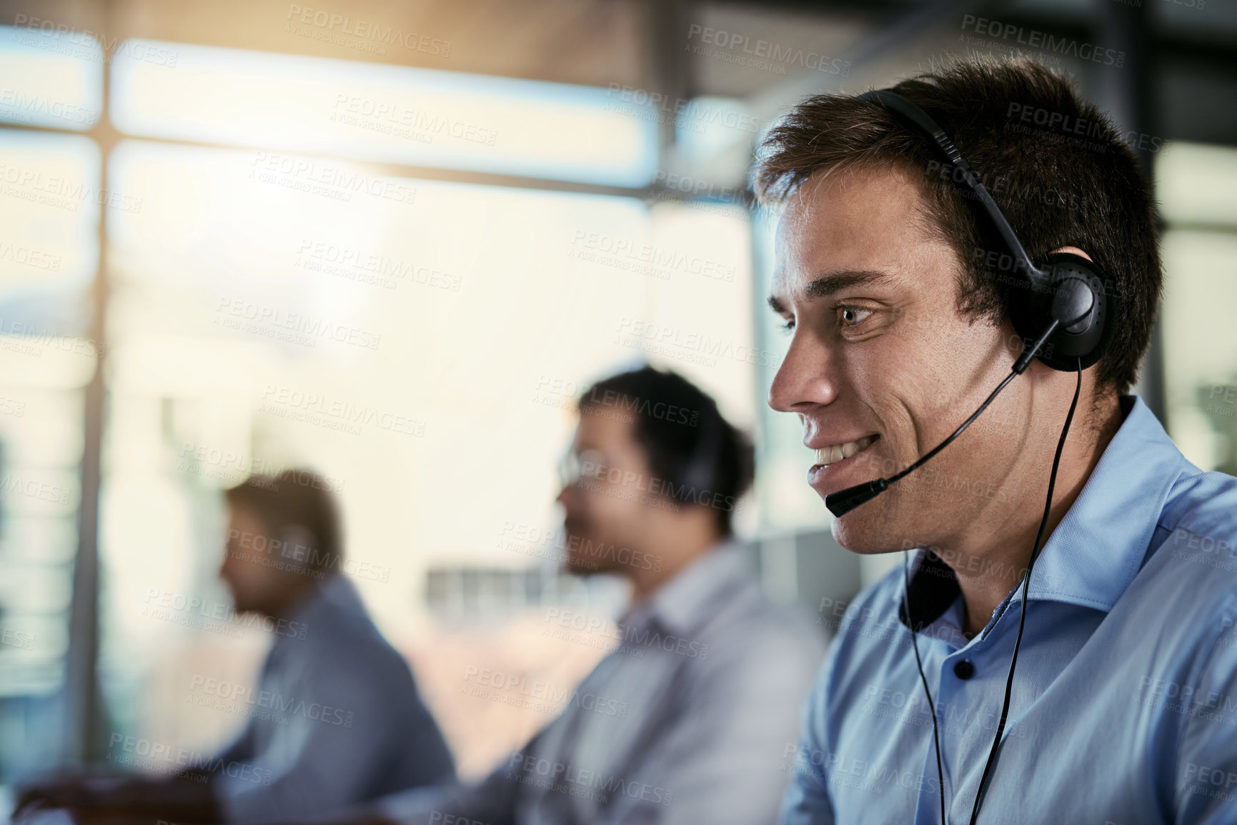 Buy stock photo Cropped shot of a call centre agent working in an office with his colleagues in the background