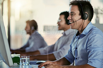 Buy stock photo Cropped shot of a call centre agent working in an office with his colleagues in the background