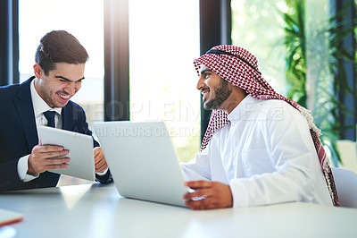 Buy stock photo Shot of a young muslim businessman using a laptop and digital tablet with his colleague at work