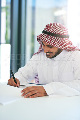 Buy stock photo Shot of a young muslim businessman writing notes at work in a modern office