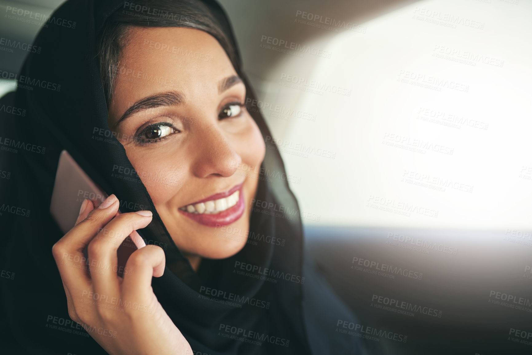 Buy stock photo Shot of a young muslim businesswoman using her phone while traveling in a car